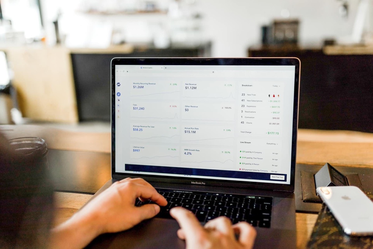 Hände tippen auf Laptop-Tastatur, Bildschirm zeigt Daten und Listen.