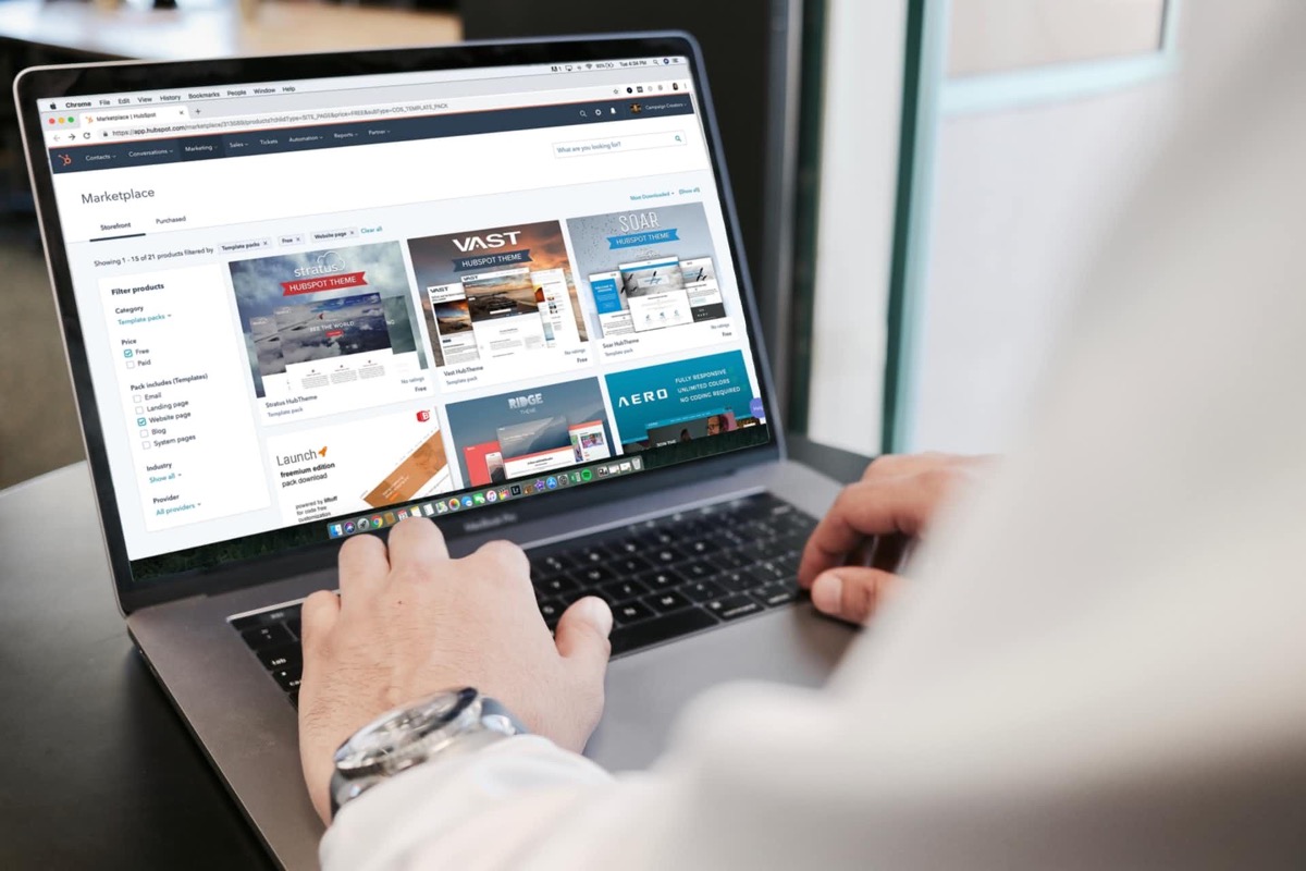 Mann tippt auf einem MacBook Pro Laptop, der eine Webseite mit Miniaturansichten von Vorlagen anzeigt.